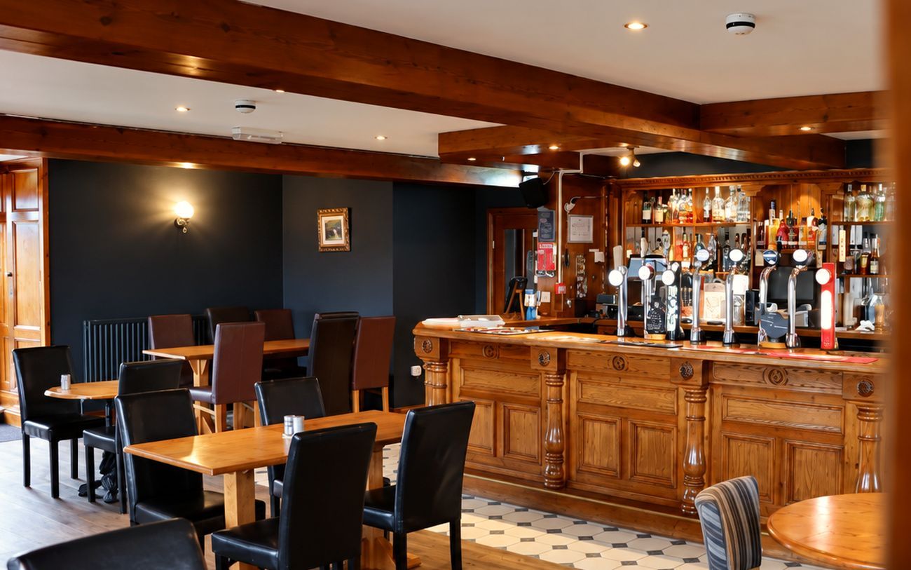 The dining room at Oily's — tables and leather chairs under the beams, the carved bar beyond