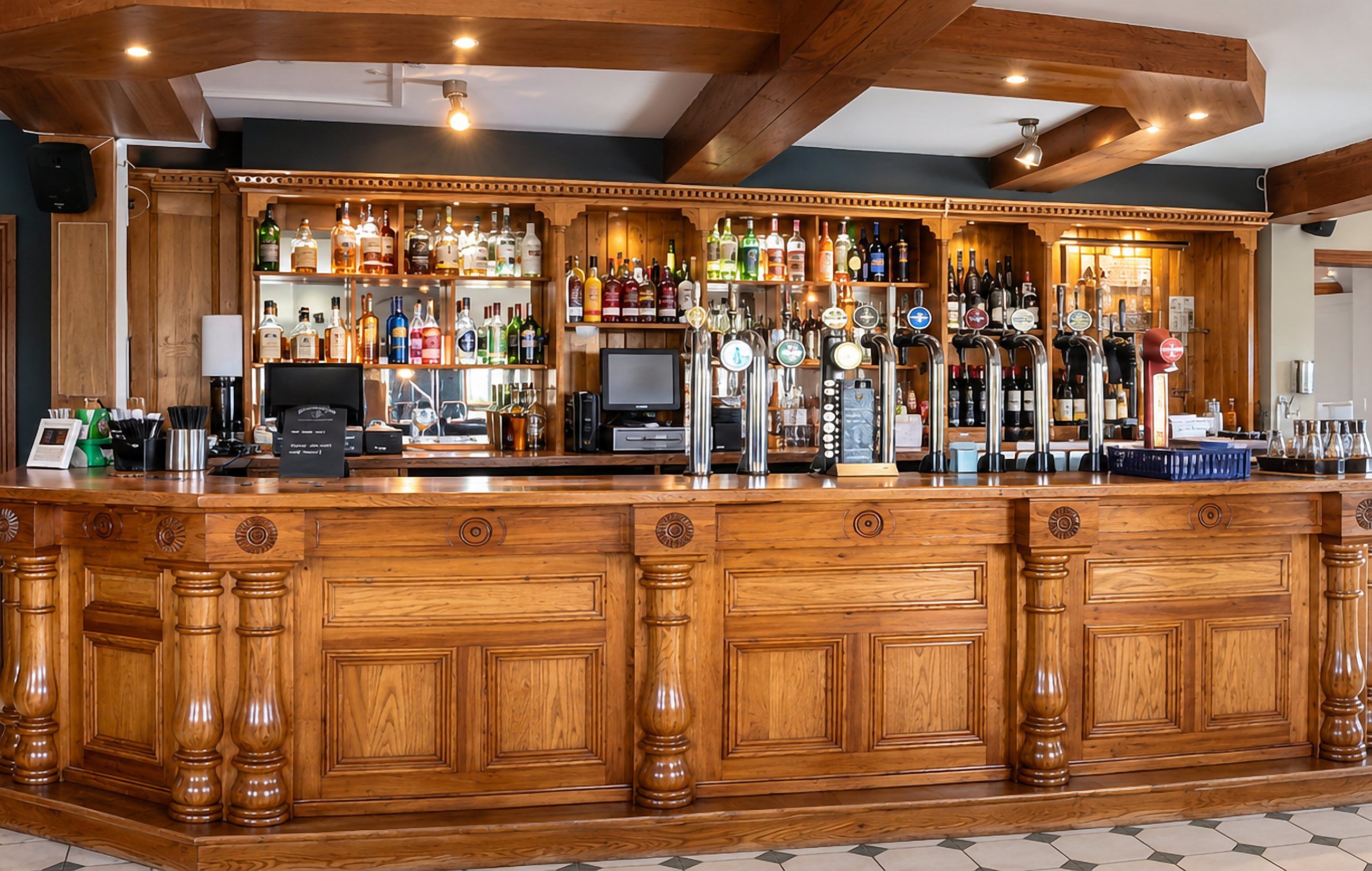 The hand-carved oak bar at Oily's — turned columns, panelled front, taps and the back shelf under the beams
