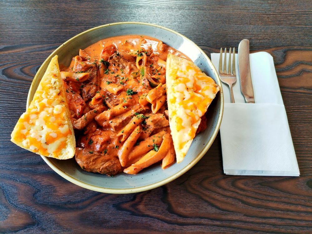 Creamy steak and pasta dish with cheesy garlic bread at Oily's